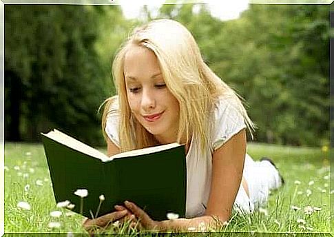 A girl reading a book in a field.