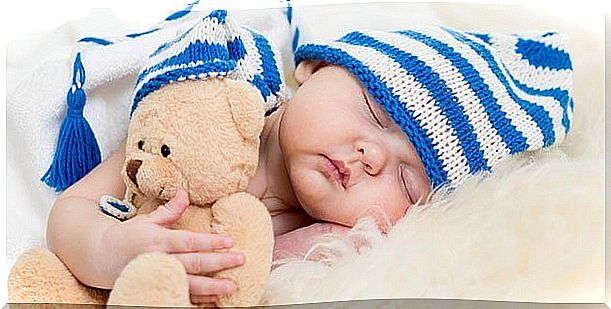 Sleeping baby with a soft toy and a hat on his head 