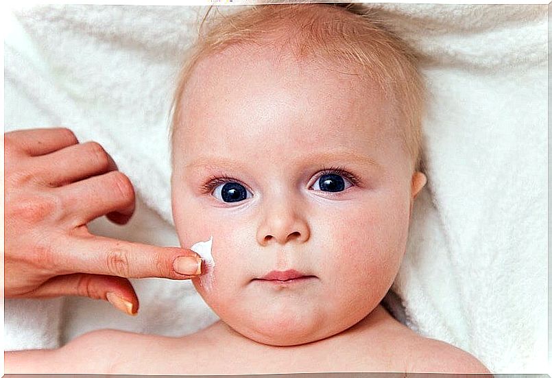 Hand passing cream on a baby's face