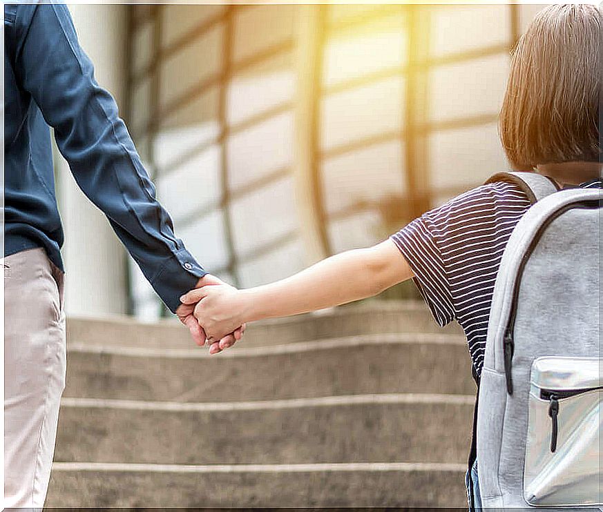 A child with a schoolbag holding an adult's hand.